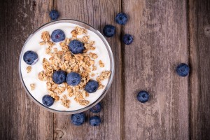 Yogurt with granola and fresh blueberries, in glass bowl over ol