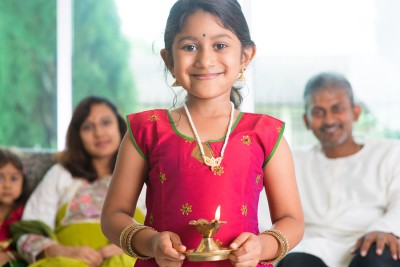 Indian family celebrate diwali or deepavali at home, little girl with traditional clothing sari, hands holding oil lamp indoor.