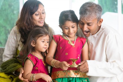 Indian family in traditional sari celebrate diwali or deepavali at home, little girl hands holding oil lamp with father indoors.