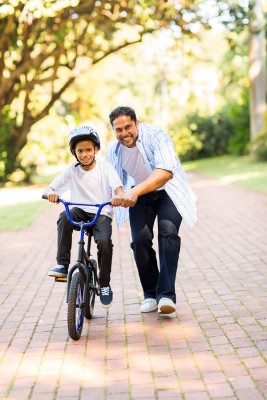 happy indian father teaching his son to ride a bicycle at the park