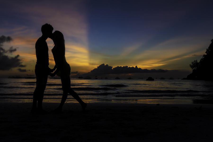 silhouettes of young loving couple kissing on tropical beach