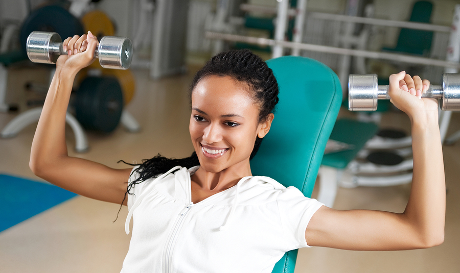 A young woman lifting free weights with a confident smile